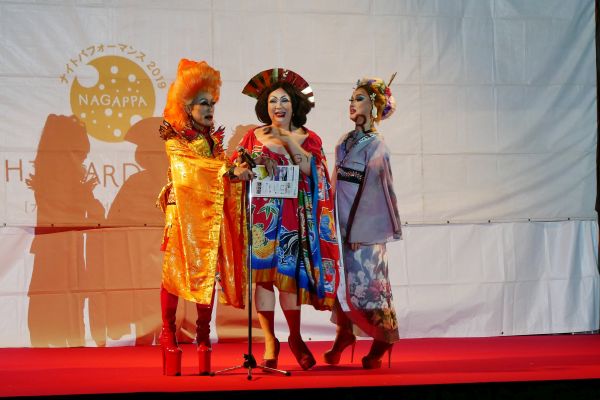 Pódium během Shinjuku gyoen night garden party, trojice travestitů zvoucí návštěvníky na další program.